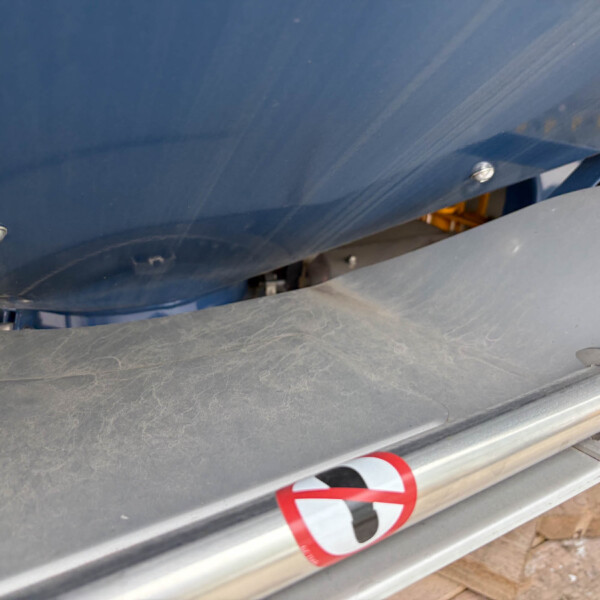 Close-up of a blue boat hull with a silver bolt and a partial red-and-white circular no-entry sign on a gray rail.