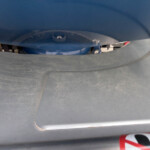 Close-up of a dark blue car bumper showing a small dent/mark and some scuffing, with a curved seam and a partial no-parking sign in the lower right corner.