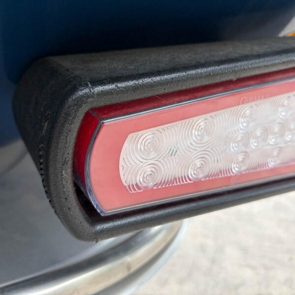 Close-up of a red taillight on a dark blue vehicle, showing a textured clear lens pattern and black housing.