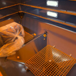 Blue metal cargo bay with orange safety rails and a plastic-wrapped bundle on a grated floor.