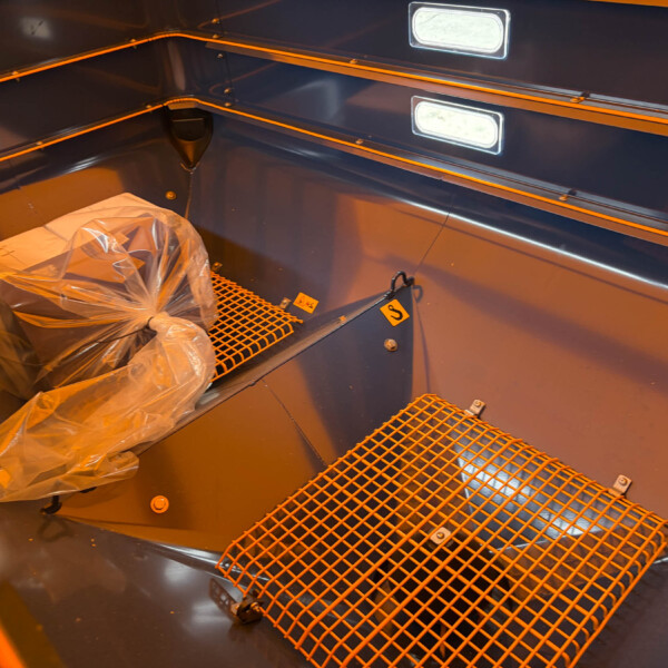 Blue metal cargo bay with orange safety rails and a plastic-wrapped bundle on a grated floor.