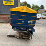 Blue industrial trailer with a yellow tarp cover labeled L20, parked on pallets in an outdoor service yard.