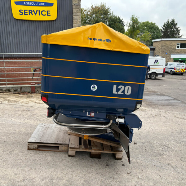 Blue industrial trailer with a yellow tarp cover labeled L20, parked on pallets in an outdoor service yard.