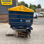 Blue L20 trailer with a yellow tarp cover resting on wooden pallets in a service yard.