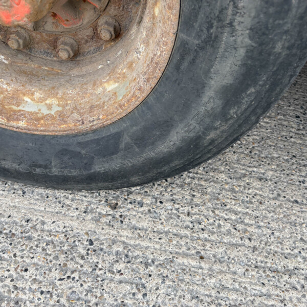 Close-up of a rusted wheel hub and worn tire on rough pavement, showing corrosion and bolts at the wheel's edge