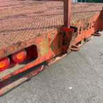 Rusty red flatbed trailer with a diamond-plate surface and row of round orange taillights along the edge