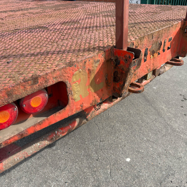 Rusty red flatbed trailer with a diamond-plate surface and row of round orange taillights along the edge