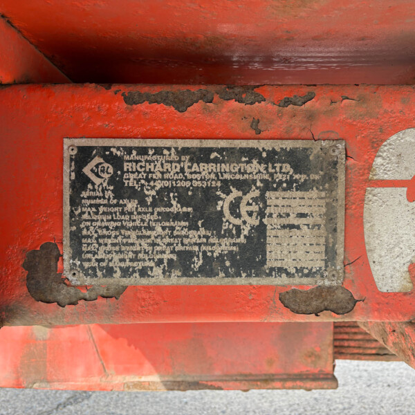 Close-up of a red, rust-streaked metal surface with a weathered black identification plate and peeling paint surface.