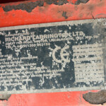 Close-up of a weathered metal nameplate on orange machinery; the white text is heavily worn and mostly illegible under chipped paint.