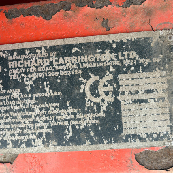Close-up of a weathered metal nameplate on orange machinery; the white text is heavily worn and mostly illegible under chipped paint.