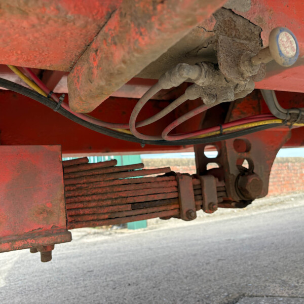 Underbelly of red farming equipment with dusty hoses and bolts, showing metal frame and components.