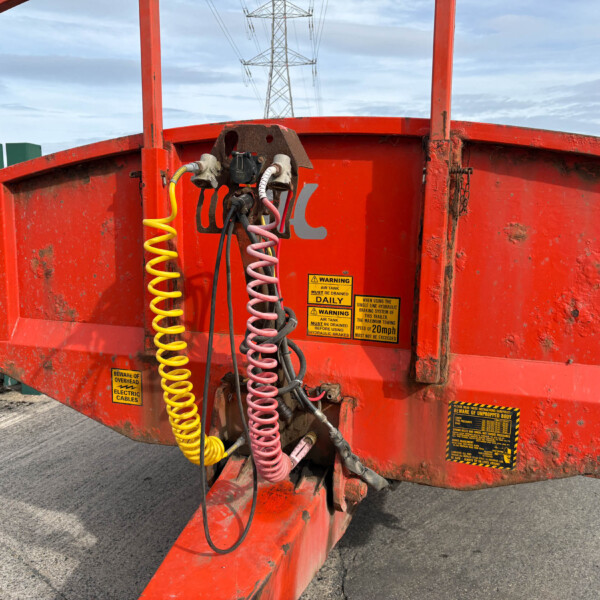 Rear of a red industrial trailer with coiled yellow and pink hoses and warning labels, outdoors near a green fence.