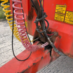 Close-up of yellow and pink spiral hydraulic hoses attached to a red industrial vehicle with warning stickers outdoors.