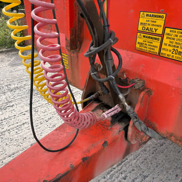 Close-up of yellow and pink spiral hydraulic hoses attached to a red industrial vehicle with warning stickers outdoors.