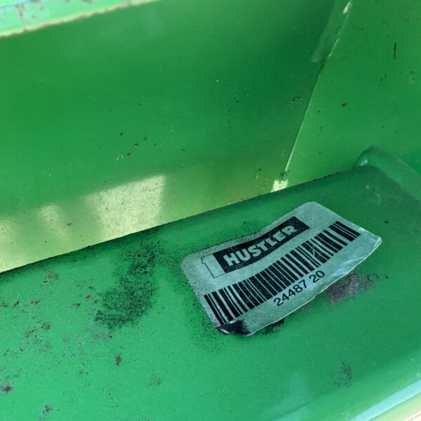 Close-up of a green metal surface with a worn barcode label partially readable as 'HUS...' and scattered dirt.
