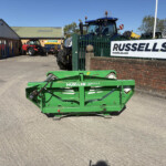 Green Hustler Unrolla LX105 mower in the foreground at a farm equipment yard, with a Russell's sign on a green fence to the right.
