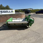Outdoor scene with a large Russell sign on a brick wall, a green machine in the foreground, and two cars parked near a modern building under a clear blue sky.
