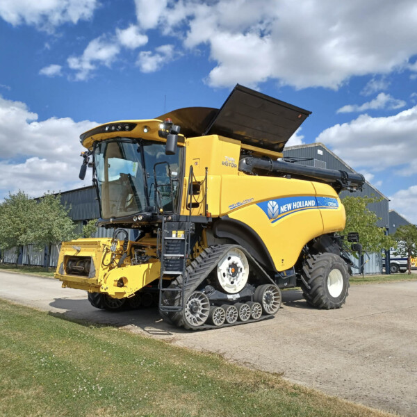 Yellow New Holland combine harvester with a raised hopper parked on a paved lot under a blue sky with scattered clouds.
