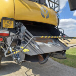 Close-up of a yellow agricultural combine with a license plate FM21 XHF, showing warning stripes and machinery components.