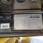Close-up of a dusty metal machinery plate showing CNH Industrial Belgium N.V. and New Holland Agriculture branding with model and specs visible.