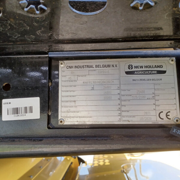 Close-up of a dusty metal machinery plate showing CNH Industrial Belgium N.V. and New Holland Agriculture branding with model and specs visible.