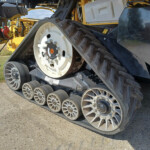 Close-up of a tracked agricultural harvester wheel and heavy rubber track on a dirt field.