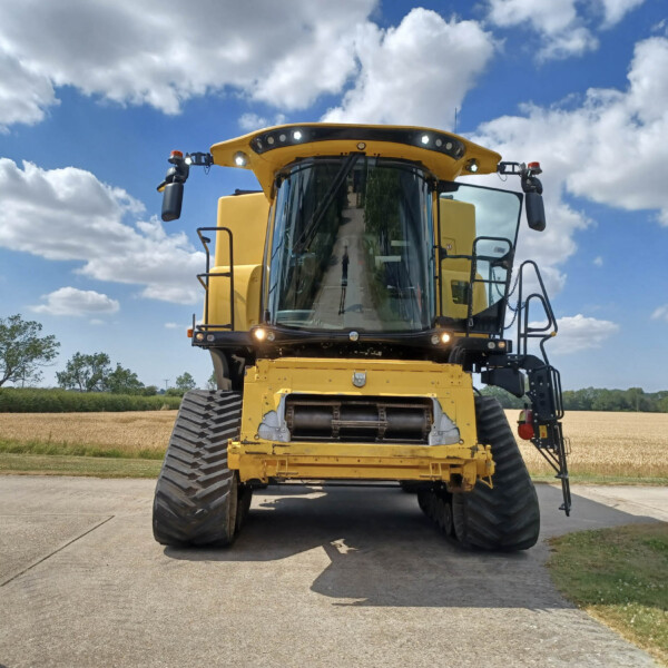 Front view of a large yellow combine harvester facing the camera on a paved road with a blue, partly cloudy sky behind it.
