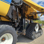 Close-up of a yellow tracked industrial machine showing gears, belts, and hydraulic components beneath the body.