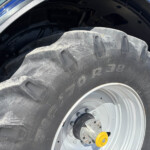 Close-up of a large tractor tire with deep treads and a gray wheel, yellow hub, and blue body in the background.