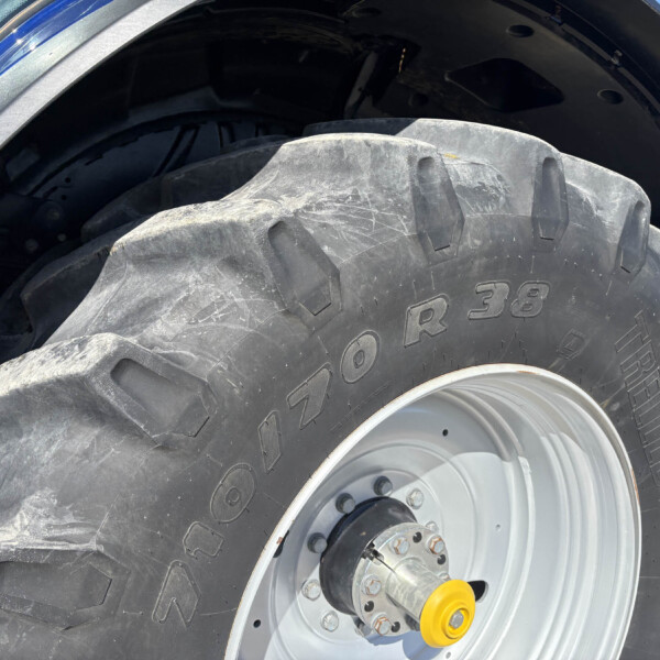 Close-up of a large tractor tire with deep treads and a gray wheel, yellow hub, and blue body in the background.