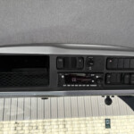 Dashboard of a vehicle cab with multiple switches and a central radio/stereo unit, gray trim and overhead console visible.