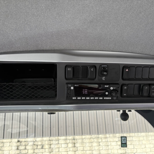 Dashboard of a vehicle cab with multiple switches and a central radio/stereo unit, gray trim and overhead console visible.