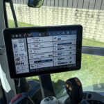 Touchscreen in a vehicle cockpit displaying engine and system diagnostics (hours, RPM, temperature, and fuel) with a rugged control joystick nearby.