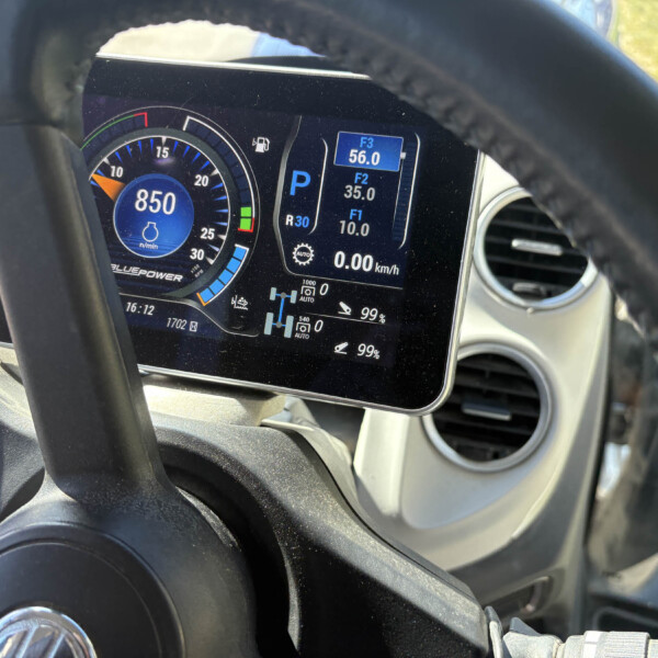 Vehicle instrument cluster visible through the steering wheel: digital tachometer around 850 rpm, gear in Park (P), and fuel/engine readouts on the right display (speed 0 km/h).