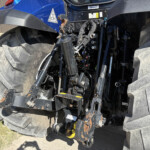 Close-up of the back of a blue tractor showing hydraulic lift arms, hitch, and oversized treaded rear tires