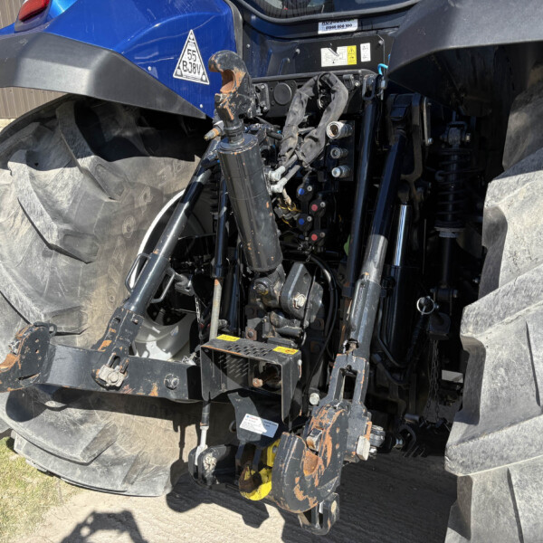 Close-up of the back of a blue tractor showing hydraulic lift arms, hitch, and oversized treaded rear tires