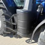 Close-up of a blue tractor cab showing the black step/ladder and a large rear tire beside it.