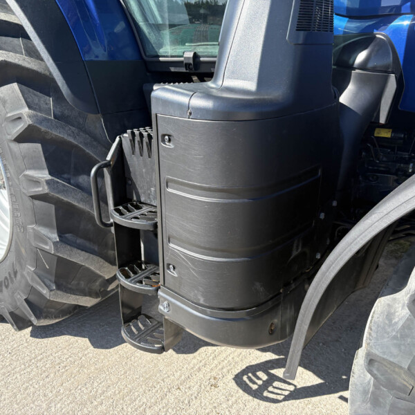 Close-up of a blue tractor cab showing the black step/ladder and a large rear tire beside it.
