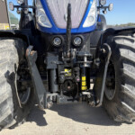 Front view of a blue agricultural tractor with oversized tread tires and dual headlights at the front center.