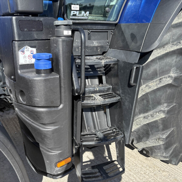 Close-up of a blue semi-truck cab showing black steps, trailer-side paneling, and a blue-capped reservoir near the door area.