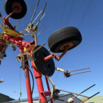 Close-up of weathered electrical utility equipment with red metal framework, gears, and large black tires against a blue sky.