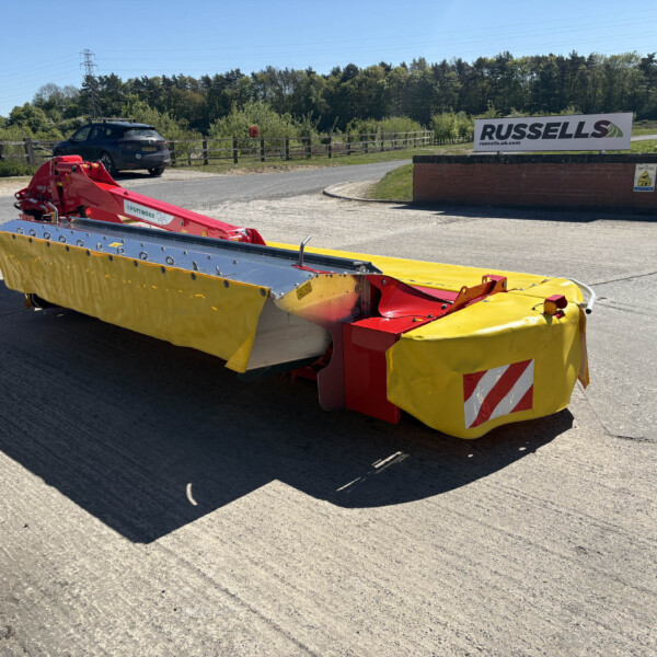 Close-up of a large yellow and red industrial roadwork mower or barrier attachment on a trailer, with a brick wall and Russell's sign in the background.