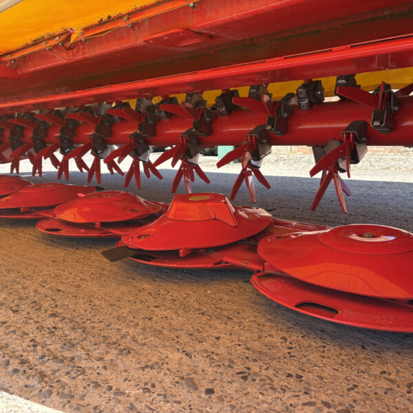 Red agricultural implement with multiple rotating blades mounted under an orange canopy, stored outdoors