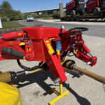 Close-up of red hydraulic construction machinery with hoses and gauges, mounted on a trailer outdoors by a road.
