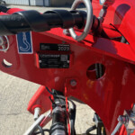 Close-up of a red farming machine hitch with a silver ring, hydraulic hoses, and a 2023 model plate visible on the frame.