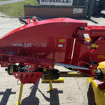 Red Novacat 402 ED mower attachment on yellow stands in a rural/farmyard setting, with other machinery in the background.