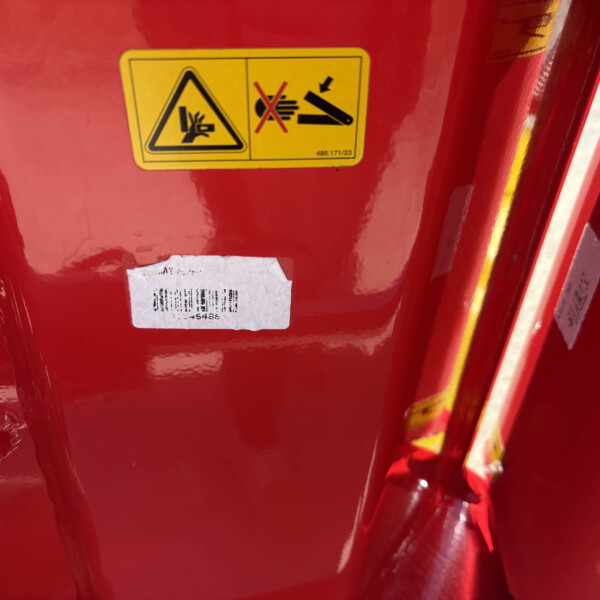 Close-up of a yellow safety label on a red surface showing hazard symbols on the left panel and a prohibition graphic on the right panel.