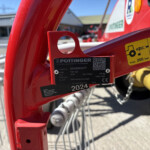 Close-up of a red farming implement frame with a yellow warning sticker and a black label showing model and QR code.