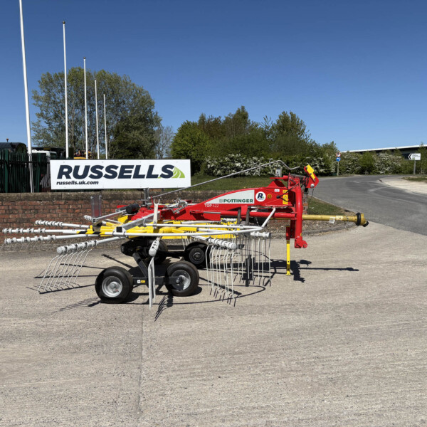 Outdoor farm equipment on display in a yard, with a Russell's sign and red machinery in the foreground under a clear blue sky.