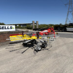 Farm equipment on a paved lot with a Russell's truck in the background and a brick wall in the foreground.